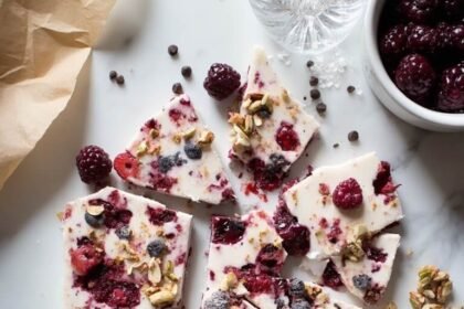 "Overhead view of high-protein frozen Greek yogurt bark with mixed berries, nuts, chocolate on a marble countertop"