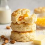 "Stack of fluffy keto biscuits made with almond flour and cheddar cheese on a white marble background, adorned with ingredients like blanched almonds and shredded cheese"