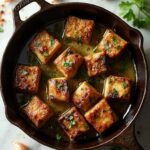 "Seared garlic butter steak bites in a cast-iron skillet with parsley and red pepper flakes on a white marble background"