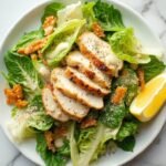 "Keto Caesar salad with homemade dressing, romaine lettuce, Parmesan crisps, grilled chicken, and a lemon wedge on a white plate against a marble background"