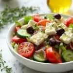 "Keto Greek salad with feta, cherry tomatoes, cucumber, red onion, green bell pepper and Kalamata olives in a white ceramic bowl on a clean marble background."