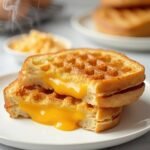 "Golden-brown keto grilled cheese sandwich with chaffle bread and melted cheddar on a white plate"