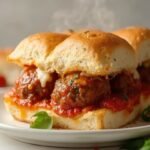 "Keto meatball sub with fathead buns, marinara, melted cheese, and fresh basil on a white plate"