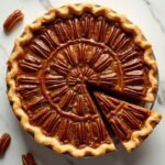 "Overhead shot of a keto pecan pie with golden caramel filling and toasted pecans on a white marble surface"