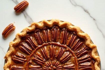 "Overhead shot of a keto pecan pie with golden caramel filling and toasted pecans on a white marble surface"