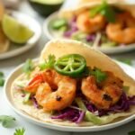 "Spicy shrimp tacos with cabbage slaw and avocado on handmade coconut tortillas, served on clean white plates and a marble surface, under soft natural light"