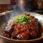 "Sugar-free Korean BBQ short ribs with gochujang marinade on a rustic ceramic platter, garnished with scallions and sesame seeds, in warm kitchen setting"