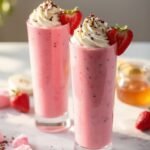 "Valentine's Day strawberry smoothies with heart-shaped strawberry garnish, whipped cream and chocolate shavings on a marble countertop"