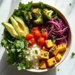 "Overhead view of a vegan keto buddha bowl with golden turmeric tofu, roasted vegetables, cauliflower rice on a clean white background."
