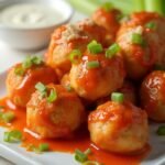 "Buffalo chicken meatballs with tangy orange sauce, garnished with green onions and celery leaves, on a white background"