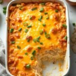 "Overhead view of buffalo ranch chicken casserole with melted cheddar and cauliflower rice, garnished with green onions, on a clean marble countertop"