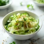"Keto Asian cucumber salad with sesame dressing in a white ceramic bowl on a clean marble surface"