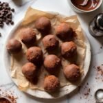 "Overhead view of keto chocolate truffles with cocoa powder on a white marble surface, surrounded by ingredients and baking tools in soft, warm lighting"