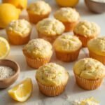 "Freshly baked keto lemon poppy seed muffins with almond flour and fresh lemons on a clean white marble background"