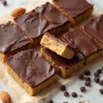 "Overhead shot of homemade keto protein bars with almond butter base and dark chocolate topping on a white marble surface"