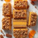 "Keto pumpkin cheesecake bars with pecan crumble on a white marble background, garnished with whole pecans, cinnamon sticks, and fresh pumpkin slices"