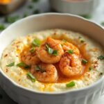 "Cauliflower grits with Cajun seasoned shrimps, cheddar cheese and scallions in a white bowl on a marble countertop, with ingredients in the background"
