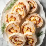 "Keto turkey and cheese pinwheels with cream cheese, bacon and cheddar on a white platter, garnished with dill sprigs"