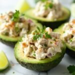 "Stuffed avocados with creamy chicken salad and lime garnish on a white marble background"