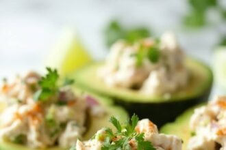 "Stuffed avocados with creamy chicken salad and lime garnish on a white marble background"